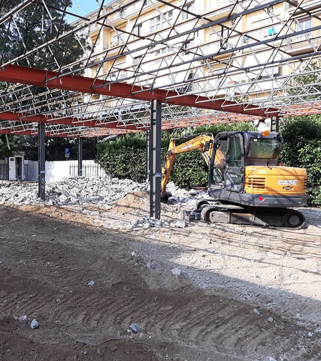 Miniescavatore giallo in demolizione pavimentazione sotto struttura metallica.